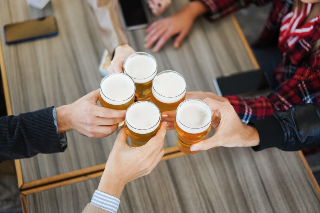 Group of people having fun cheering with beer inside brewery bar - Focus on glasses